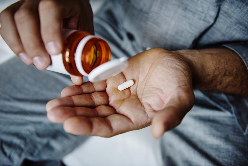 Man taking medicine, pill bottle and pill in hand