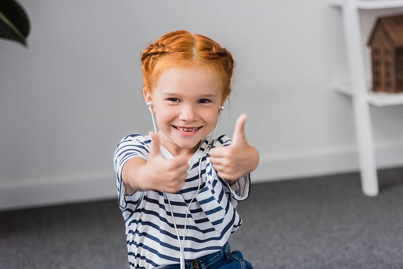 happy little girl listening music and showing thumbs up